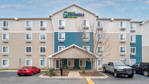 A multi-story hotel with a flat facade, a prominent entrance, and a parking lot with vehicles. - Extended Stay America Select Suites - Tallahassee - East (Tallahassee)