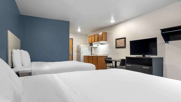 A hotel room with two beds, a kitchenette, a desk, and a TV. - Extended Stay America Select Suites - Tallahassee - East (Tallahassee)
