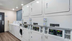 A laundry facility with multiple washing machines and dryers, control panels, and a telephone. - Extended Stay America Select Suites - Tallahassee - East (Tallahassee)