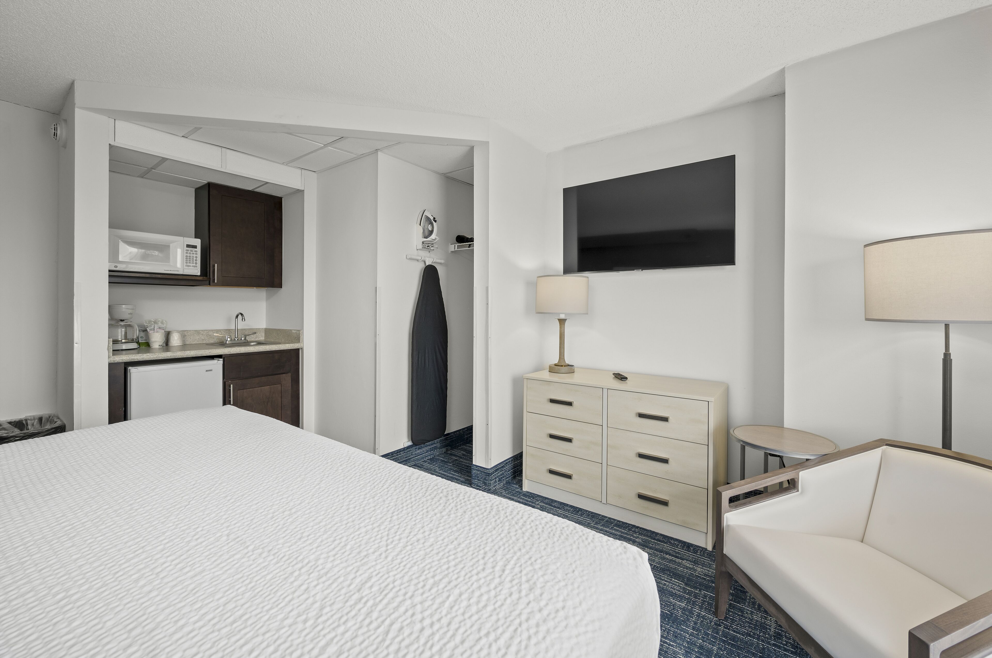 A hotel room with a large bed, a desk with a microwave, a TV, and a lamp.