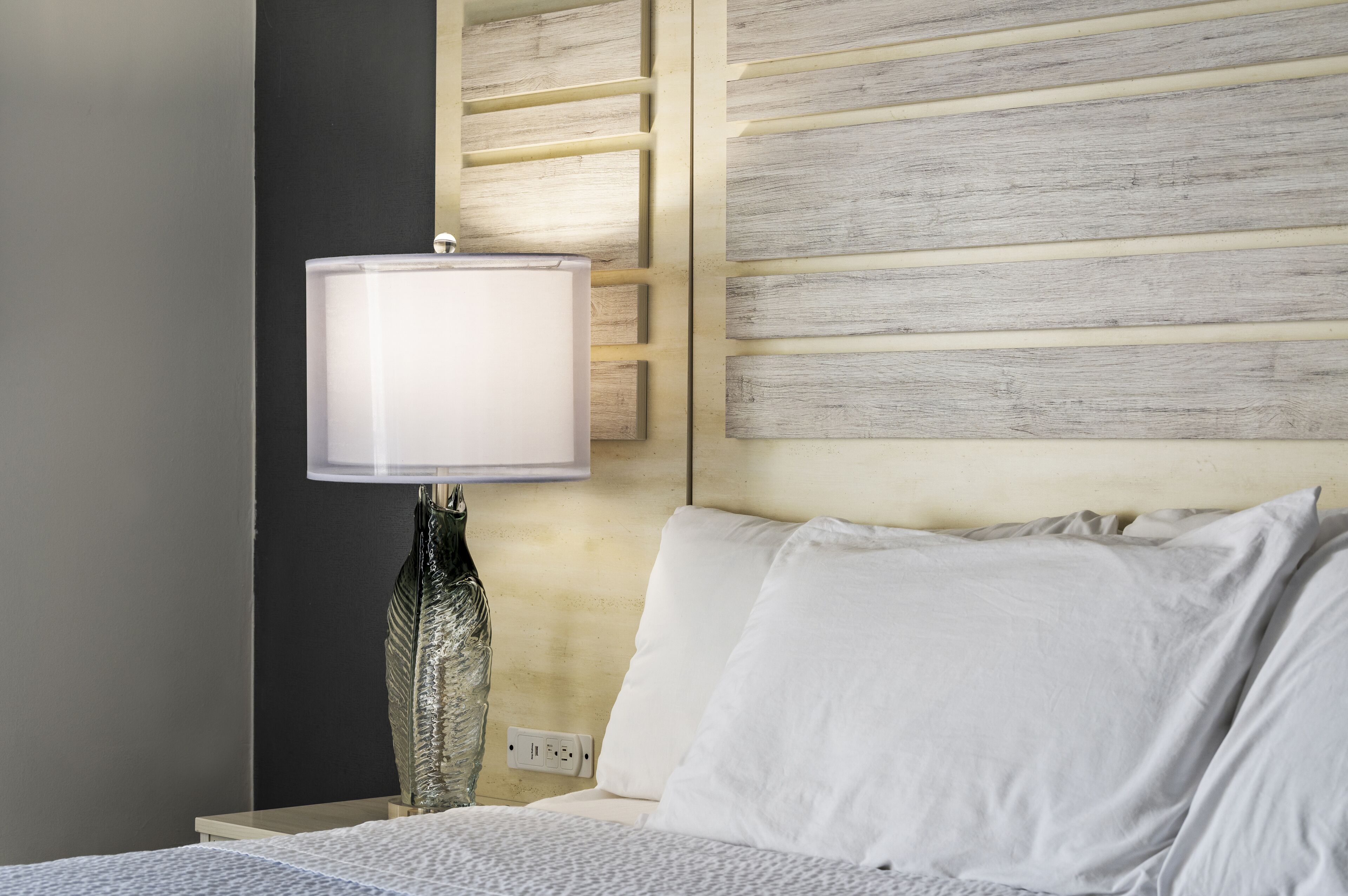 Un lit bien fait, avec du linge de lit blanc, une lampe de chevet et une tête de lit en bois.