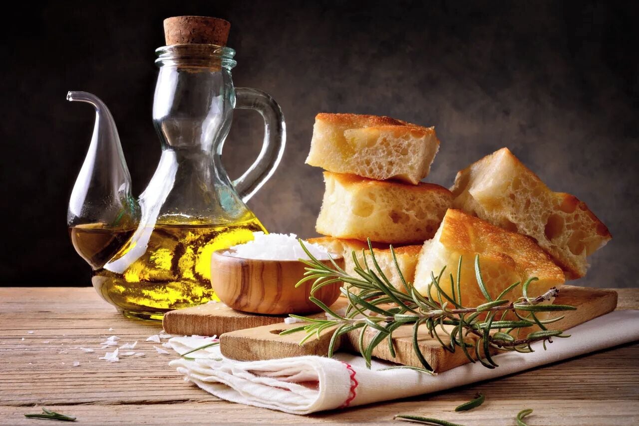 Una botella de vidrio con aceite de oliva, un cuenco de madera y trozos de pan sobre una superficie de madera.