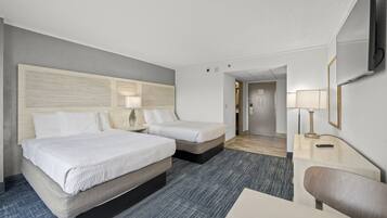 A hotel room with two beds, a desk, a chair, a TV, and a lamp.