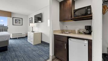 Habitación de hotel pequeña con cama, escritorio, microondas, cafetera y refrigerador.