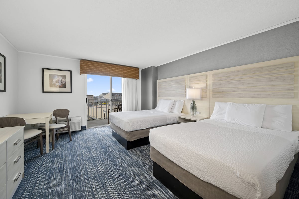 A hotel room with two beds, a desk, a chair, and a window with a view of buildings.