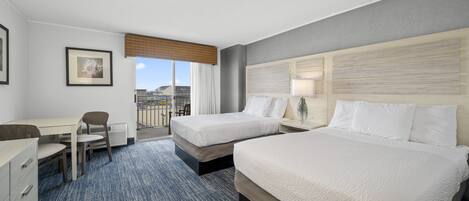 A hotel room with two beds, a desk, a chair, and a window with a view of buildings.