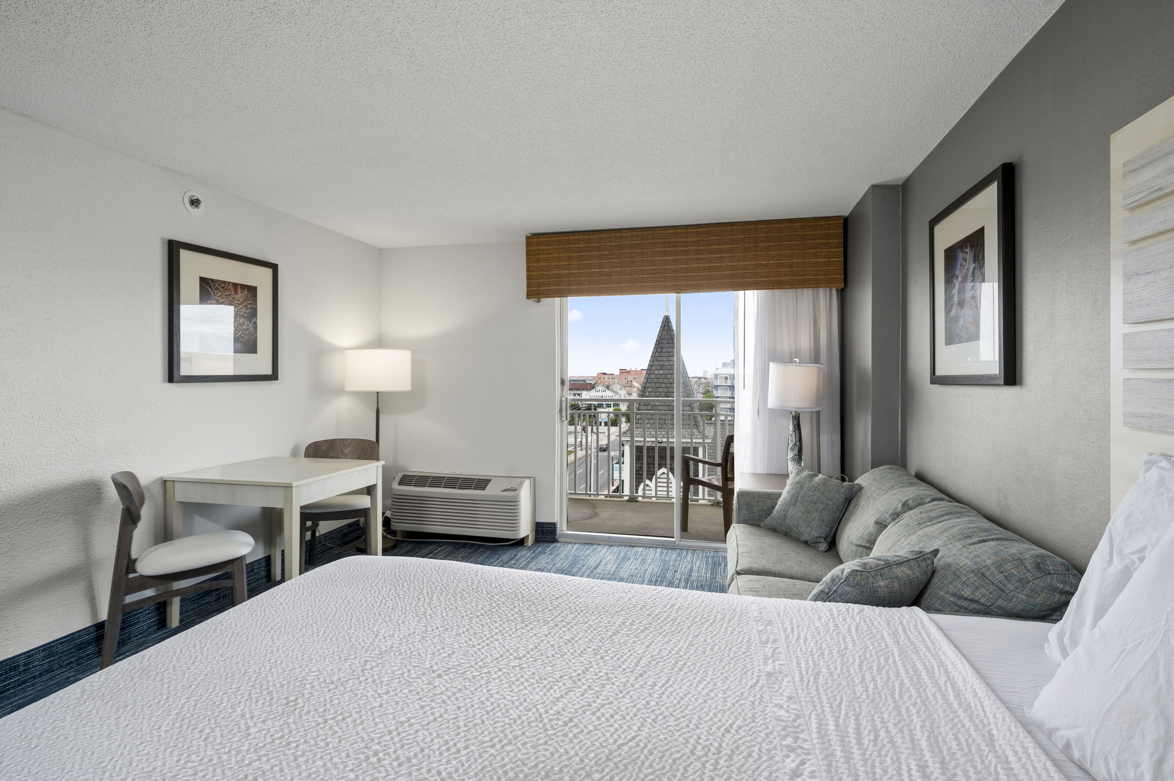 Habitación de hotel con una cama grande, un escritorio, una silla, un sofá y un balcón con vistas a edificios.
