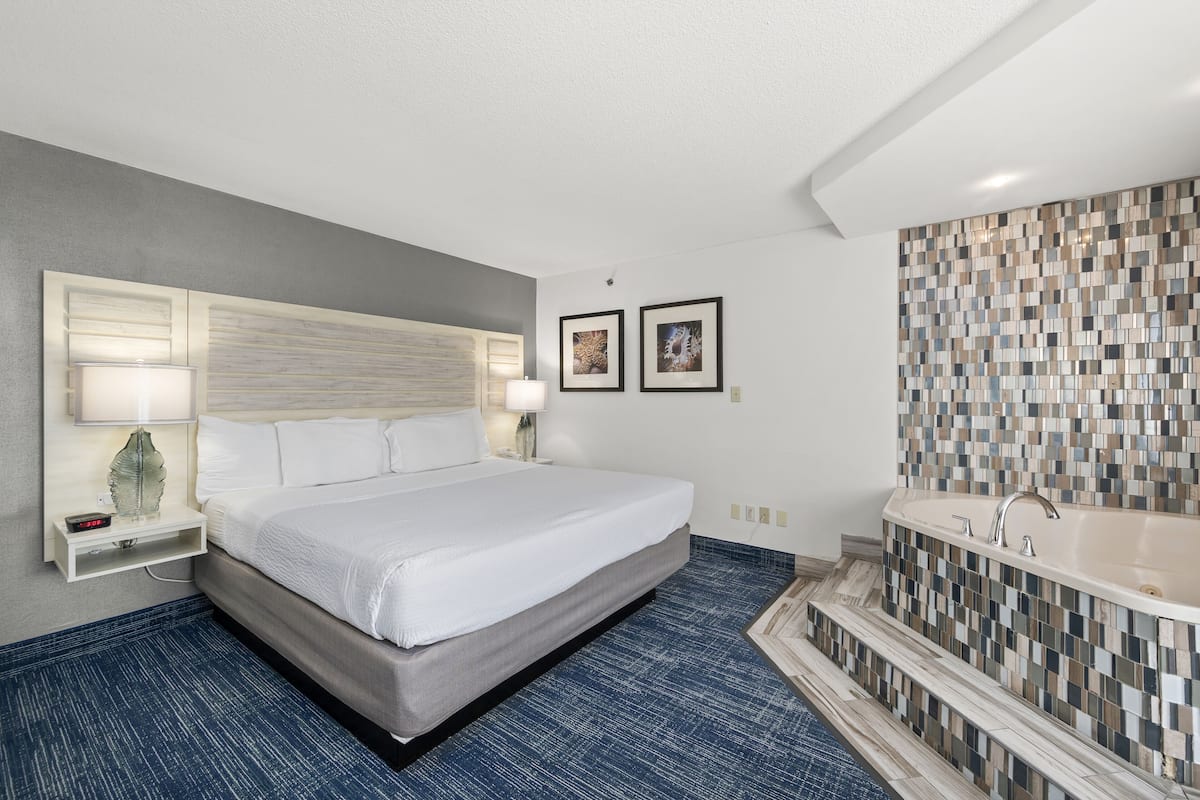 A hotel room with a large bed, a built-in bathtub, and a blue carpet.