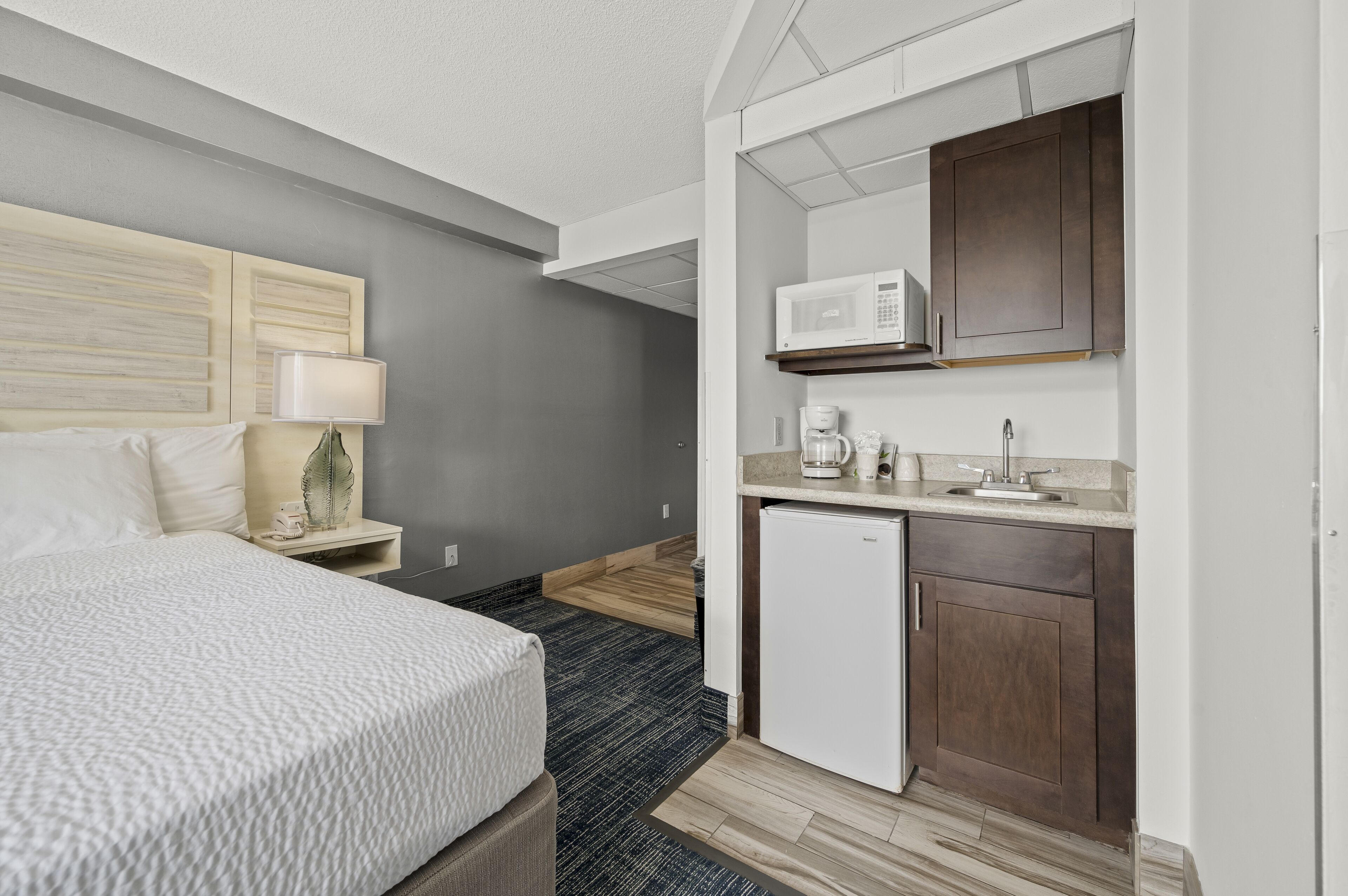Una habitación de hotel con cama, escritorio, microondas, cafetera y refrigerador.