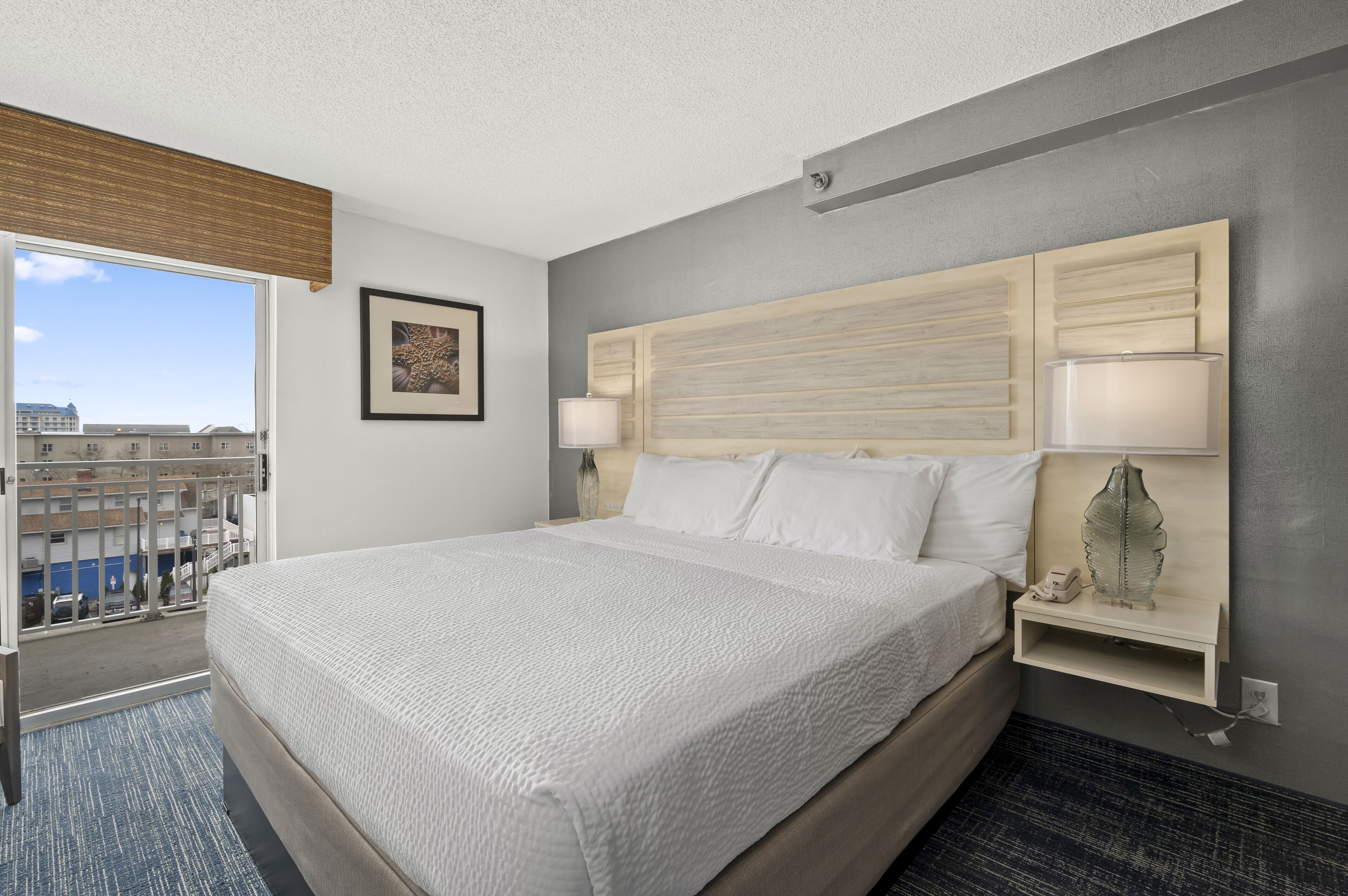 A hotel room with a large bed, bedside lamps, a nightstand, and a view of the city through a large window.