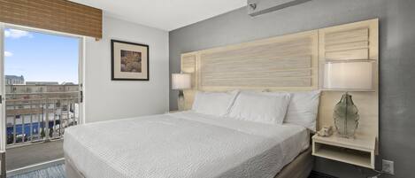 A hotel room with a large bed, bedside lamps, a nightstand, and a view of the city through a large window.