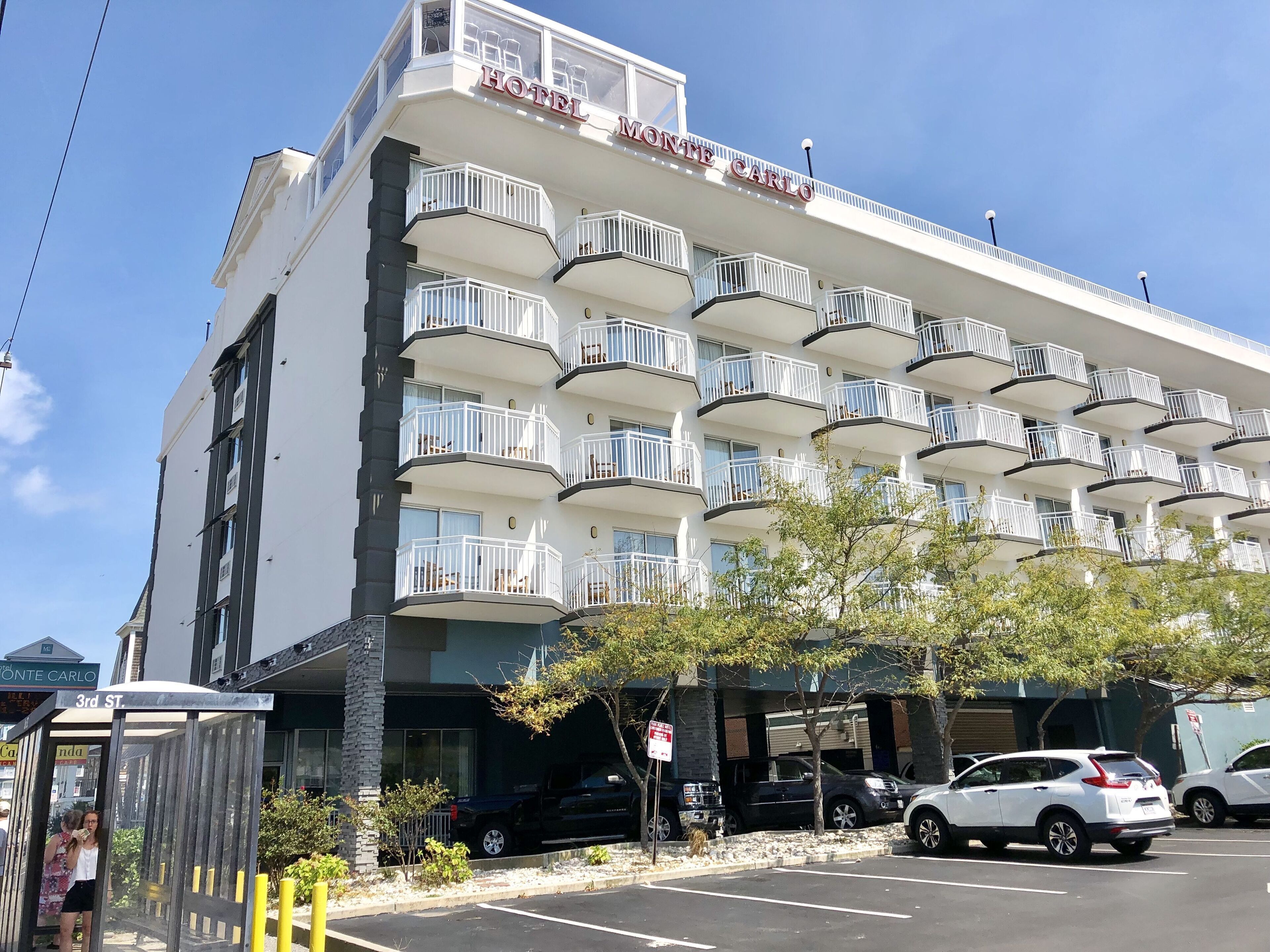Un hôtel à plusieurs étages doté de balcons, un ciel dégagé et des voitures garées.