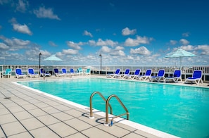 Una piscina con sillas reclinables azules y sombrillas a rayas.