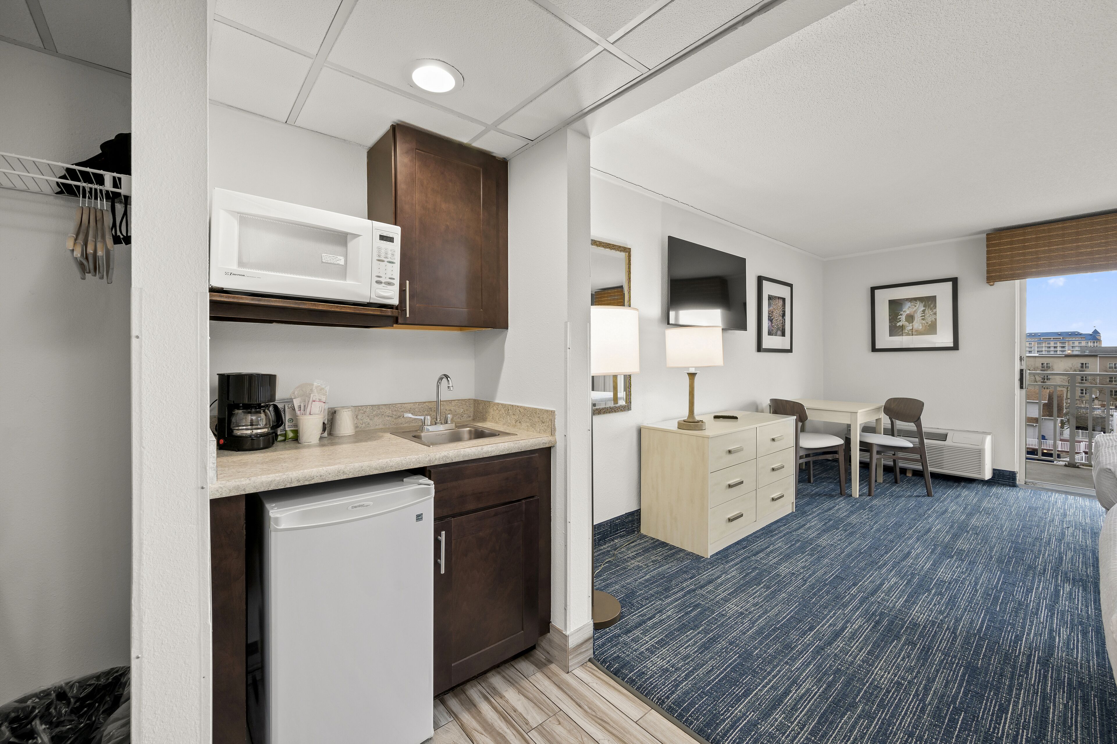 A compact hotel room with a kitchenette, a dining area, and a view of the city.