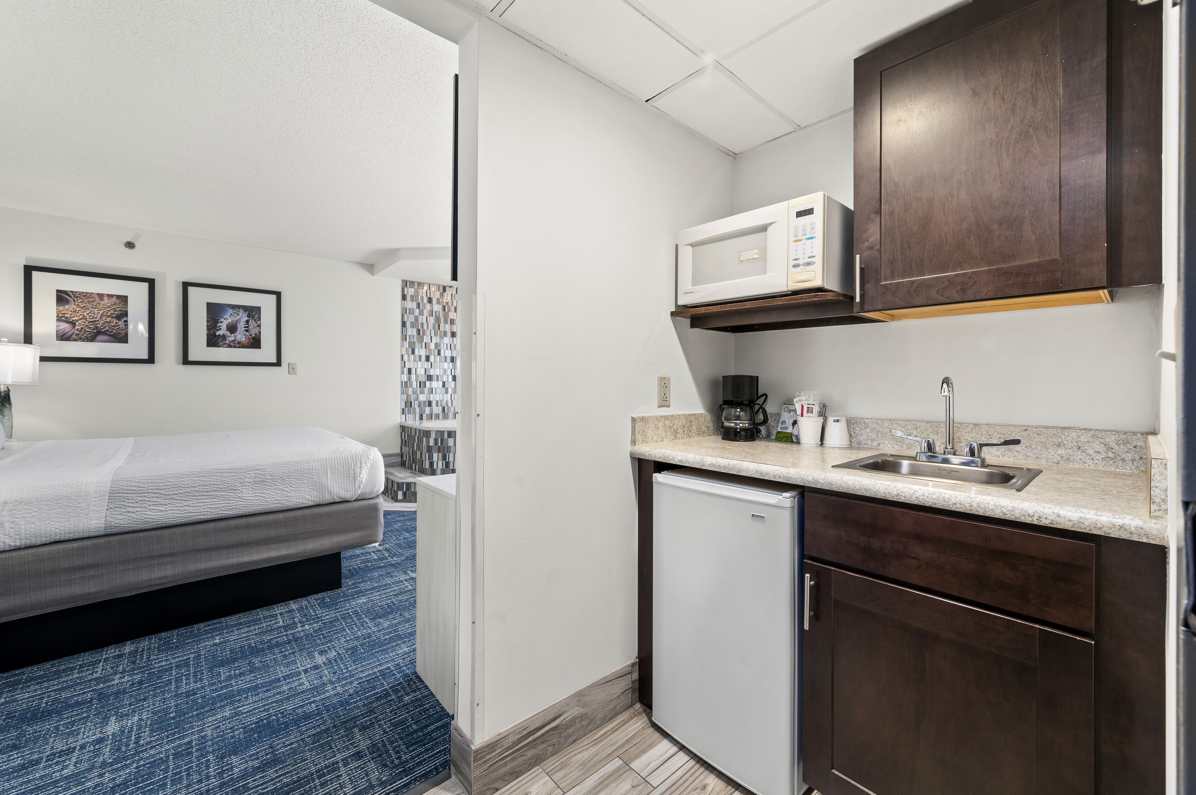 A compact hotel room with a bed, a small kitchenette, a microwave, and a sink.