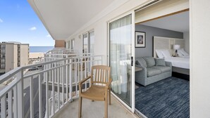 A balcony with a chair, a sliding glass door leading to a bedroom with a bed, a sofa, and a lamp. - Hotel Monte Carlo Ocean City (Ocean City)