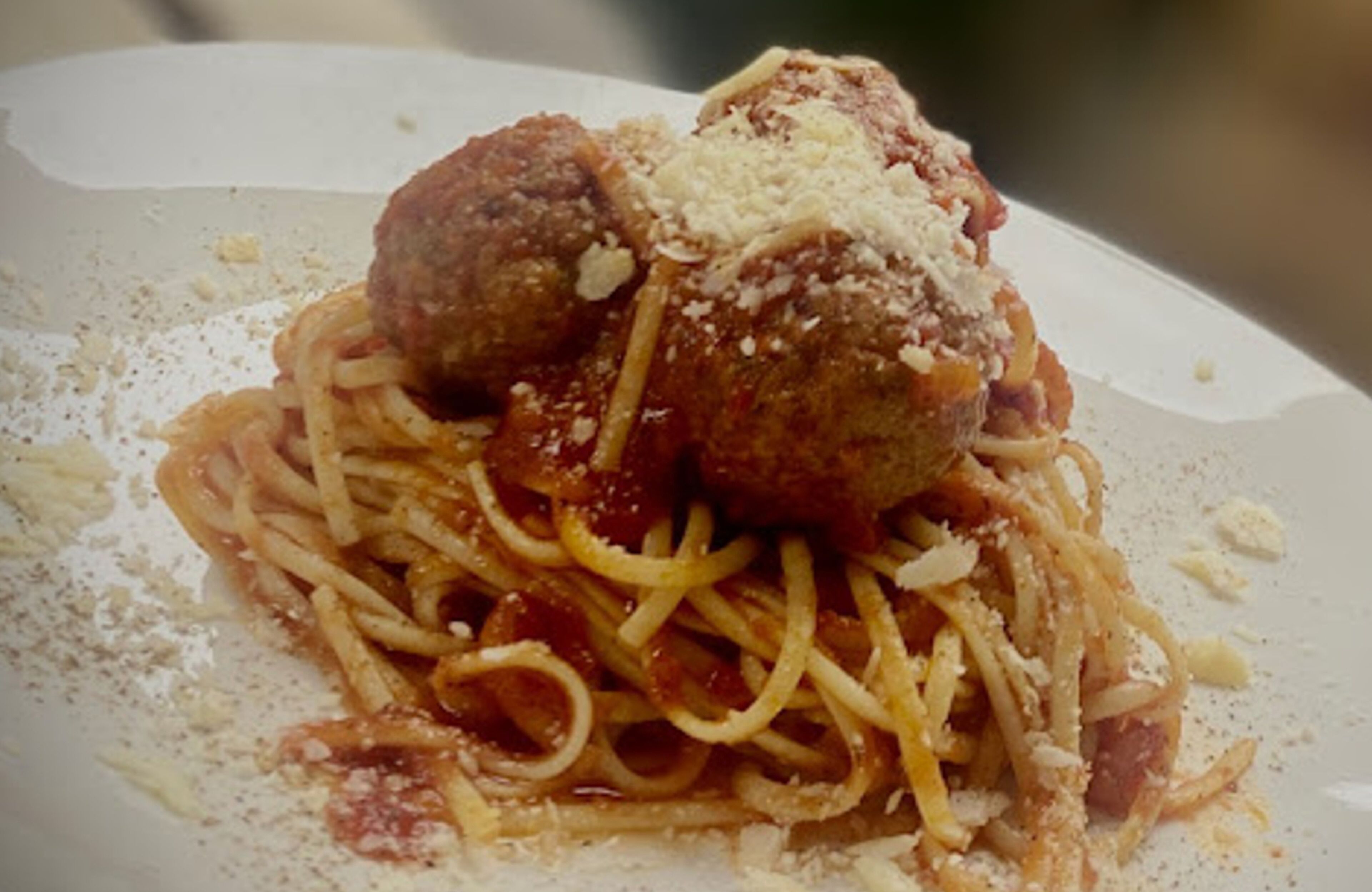 A plate of spaghetti with meatballs and grated cheese.