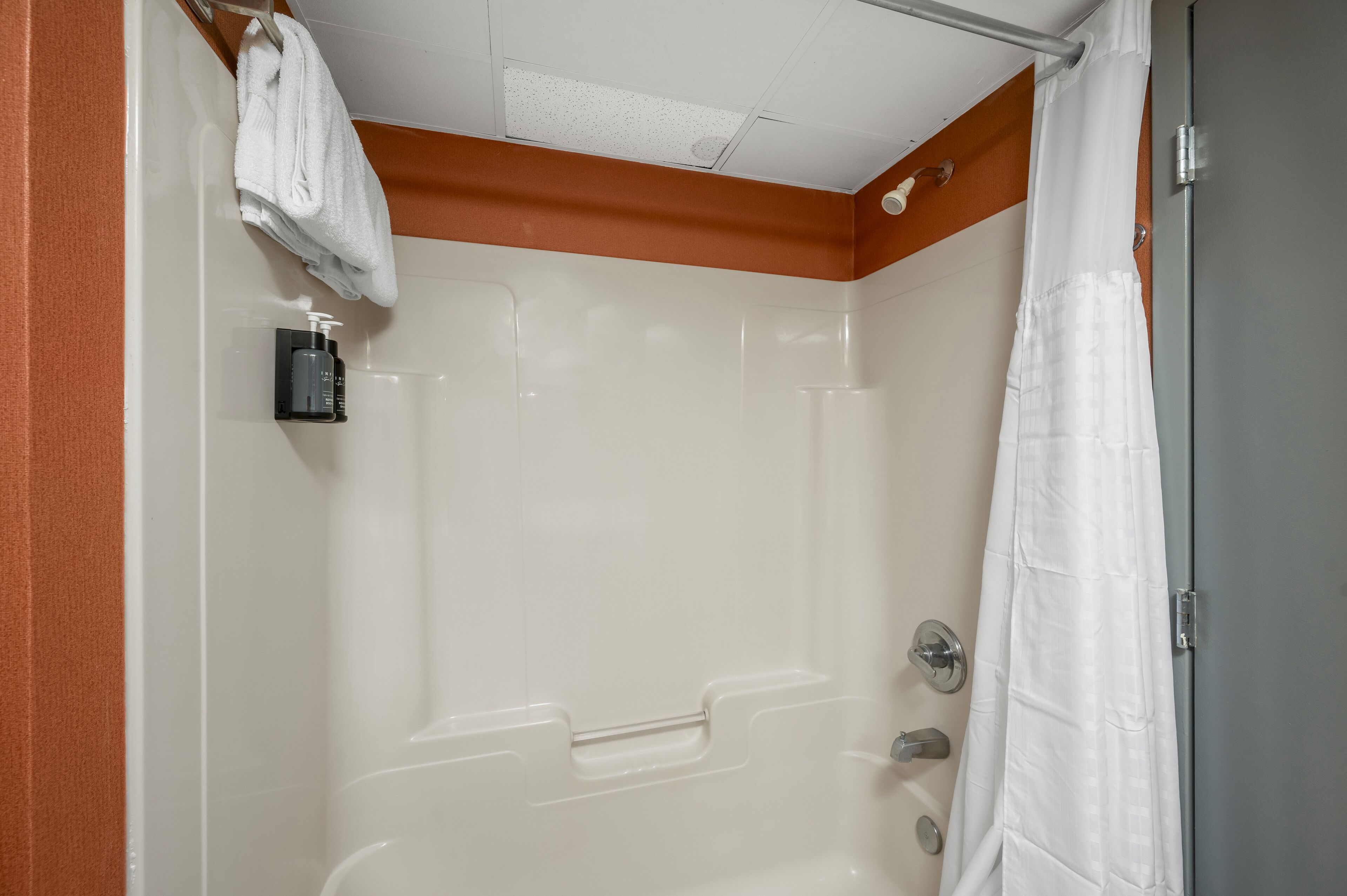 A bathroom with a shower, a towel rack, and a soap dispenser.