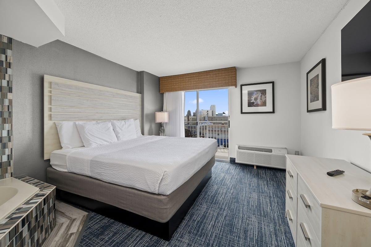 A hotel room with a large bed, a desk, a dresser, and a view of the city through the window.