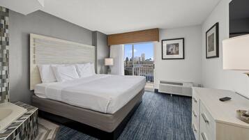 A hotel room with a large bed, a desk, a dresser, and a view of the city through the window.