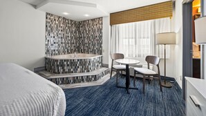 A hotel room with a large bed, a bathroom with a mosaic tile wall, a small table with two chairs, and a floor lamp. - Hotel Monte Carlo Ocean City (Ocean City)