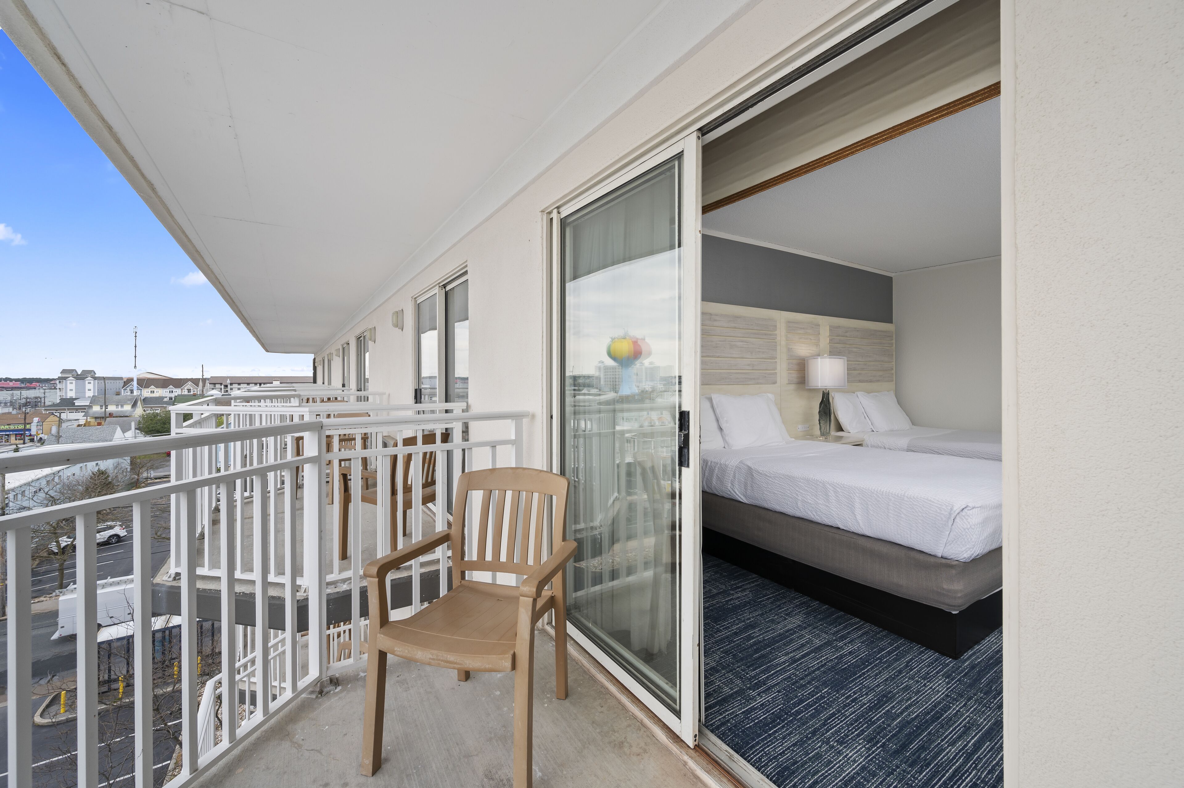 Un balcón con una silla de madera, una cama con ropa de cama blanca y vistas a la ciudad.