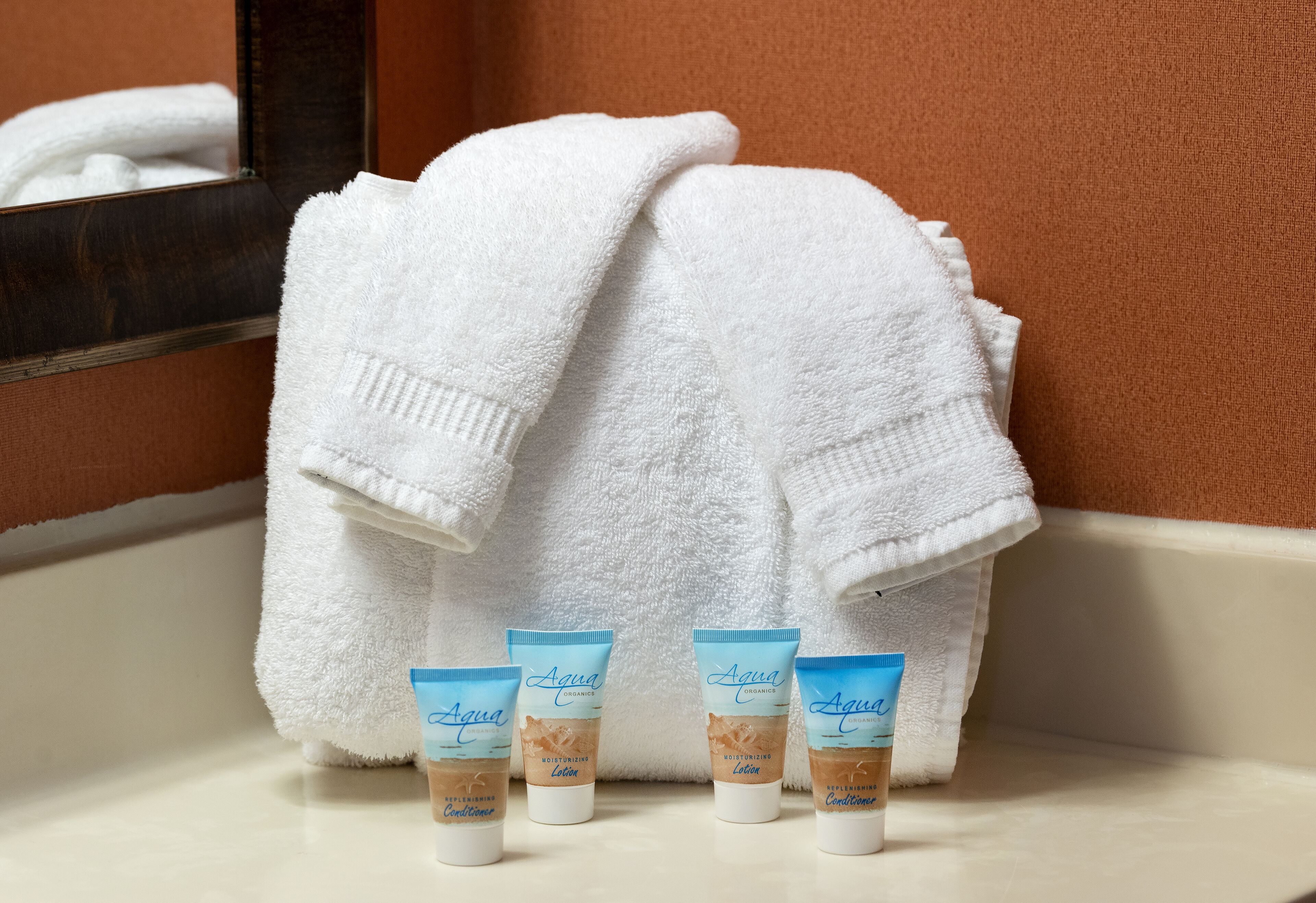 A bathroom with a white towel, a mirror, and three Aqua moisturizing lotion tubes.