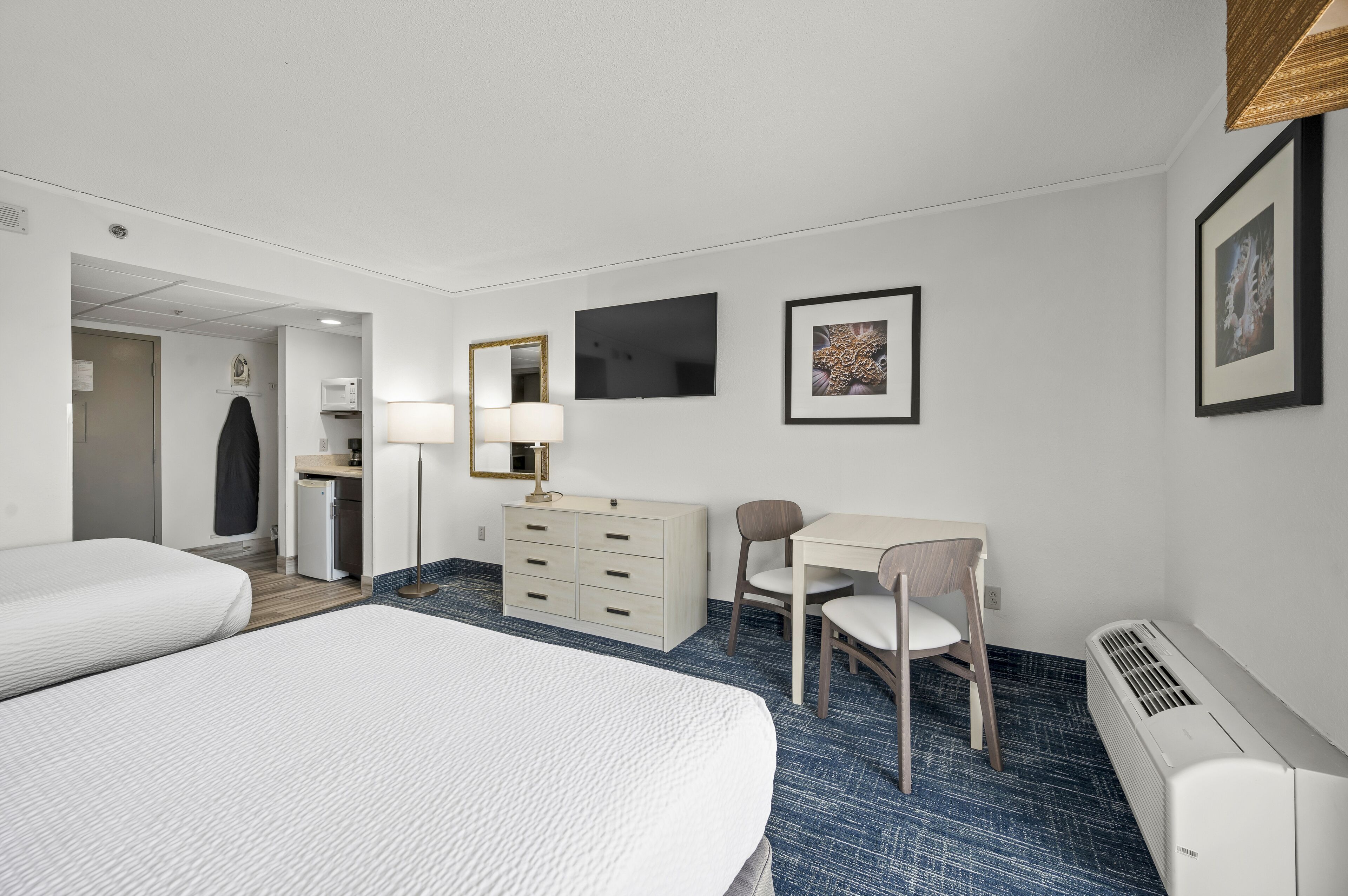 Une chambre d’hôtel avec deux lits, un bureau, une chaise, une petite kitchenette et un téléviseur.