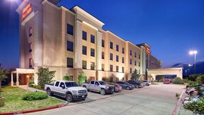 A hotel with a parking lot, multiple vehicles, and a well-lit entrance. - Hampton Inn & Suites Waco-South (Waco)