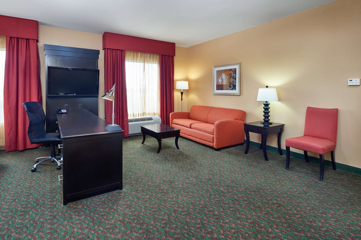 Une chambre d’hôtel équipée d’un bureau, de deux chaises, d’un canapé, d’une petite table, d’une lampe et d’un tableau au mur.