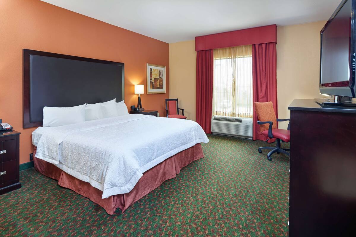 Une chambre d’hôtel avec un grand lit, un bureau avec un ordinateur, une chaise, une lampe et un téléviseur.