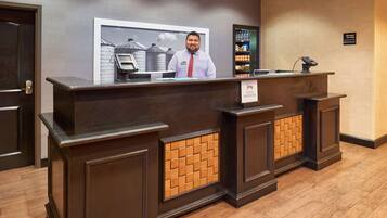 A reception desk with a framed picture above it, a sign indicating 'Manager On Duty', and a display of bottled water and snacks.