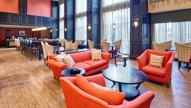 A spacious lobby with a mix of seating options including sofas and chairs, a central coffee table, and a bar area in the background. - Hampton Inn & Suites Waco-South (Waco)