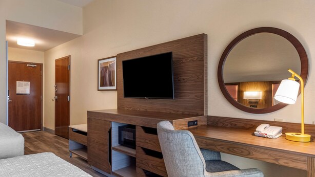 Habitación de hotel con un escritorio de madera, televisor, espejo, lámpara y cama.