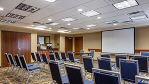 Un salón de conferencias con filas de sillas, una pantalla de proyector y suelo alfombrado.