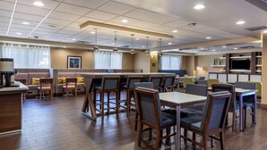 Comedor de hotel con mesas y sillas de madera, una zona de bar y un televisor.