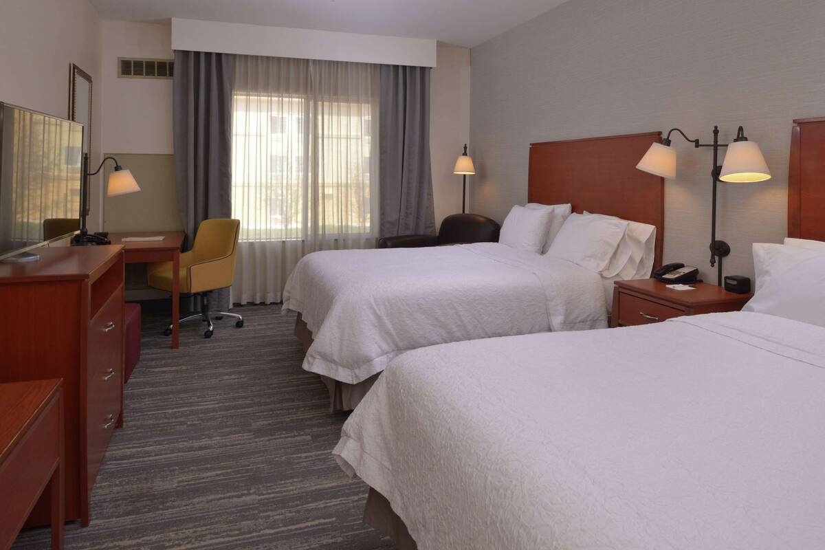Ein Hotelzimmer mit zwei Betten, einem Schreibtisch, einem Stuhl und einem Nachttisch mit Lampen.