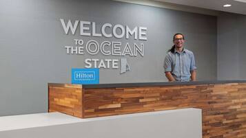 En receptionsdisk med en skylt som lyder ”Välkommen till Ocean State” och en Hilton-logotyp.