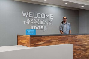 A reception desk with a "Welcome to the Ocean State" sign and a Hilton logo.