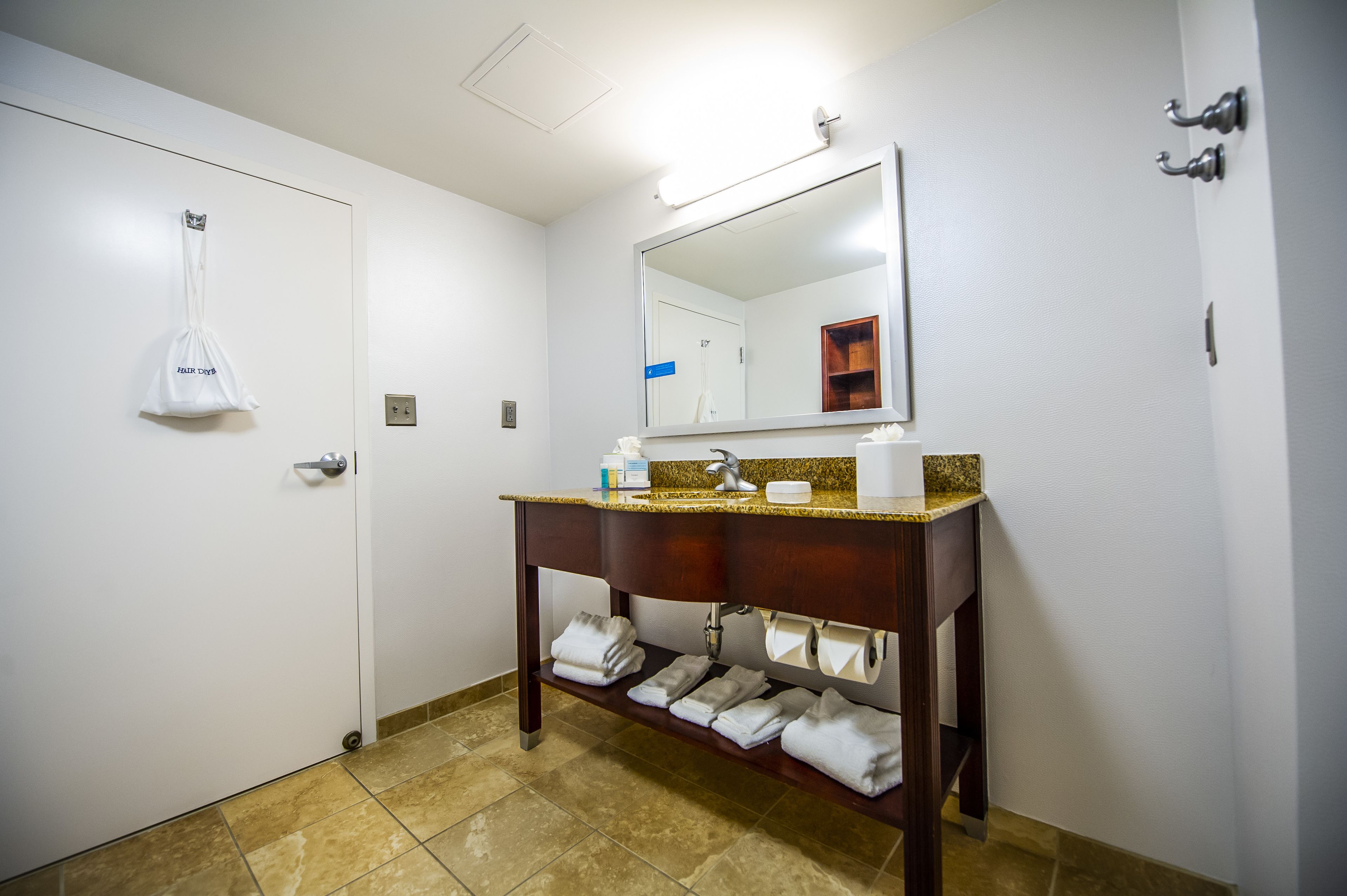 A hotel bathroom with a white door, a mirror above the sink, and towels on the floor.
