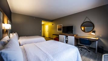 A hotel room with two beds, a desk, a television, and a mirror.