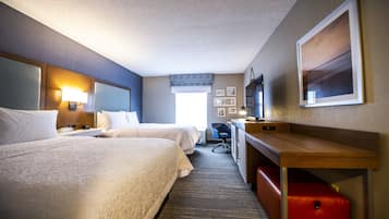 A hotel room with two beds, a desk, a chair, a TV, and a window with a view.