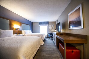A hotel room with two beds, a desk, a chair, a TV, and a window with a view.
