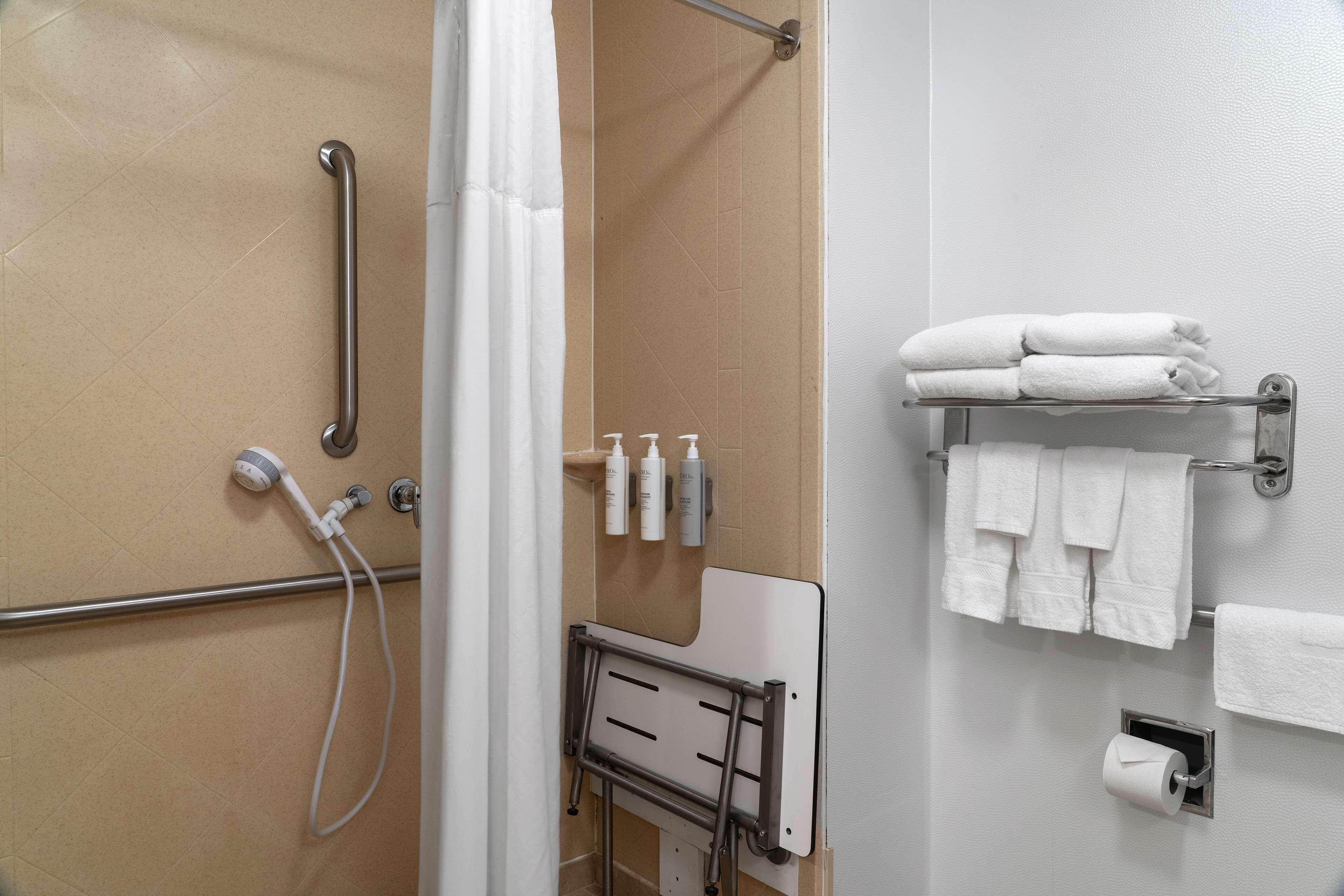A bathroom with a shower, grab bars, a towel rack, and toiletries.