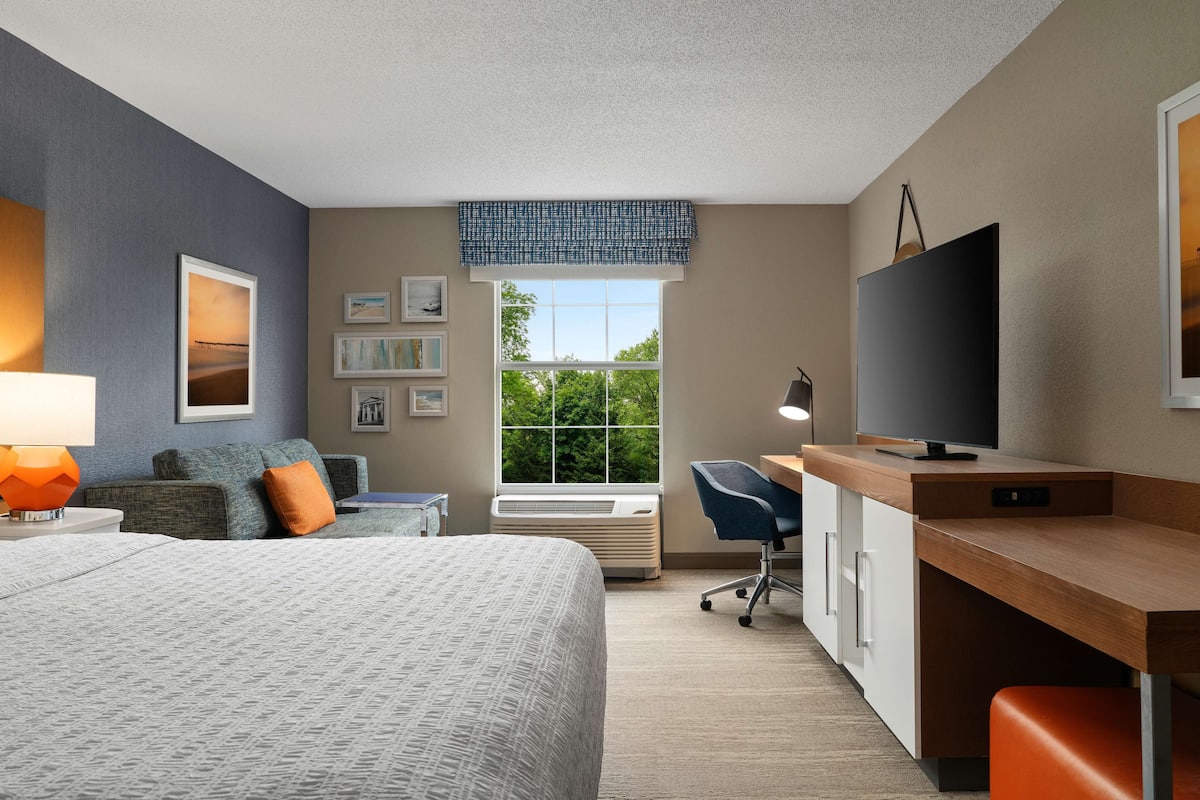 A modern hotel room with a bed, desk, and TV.