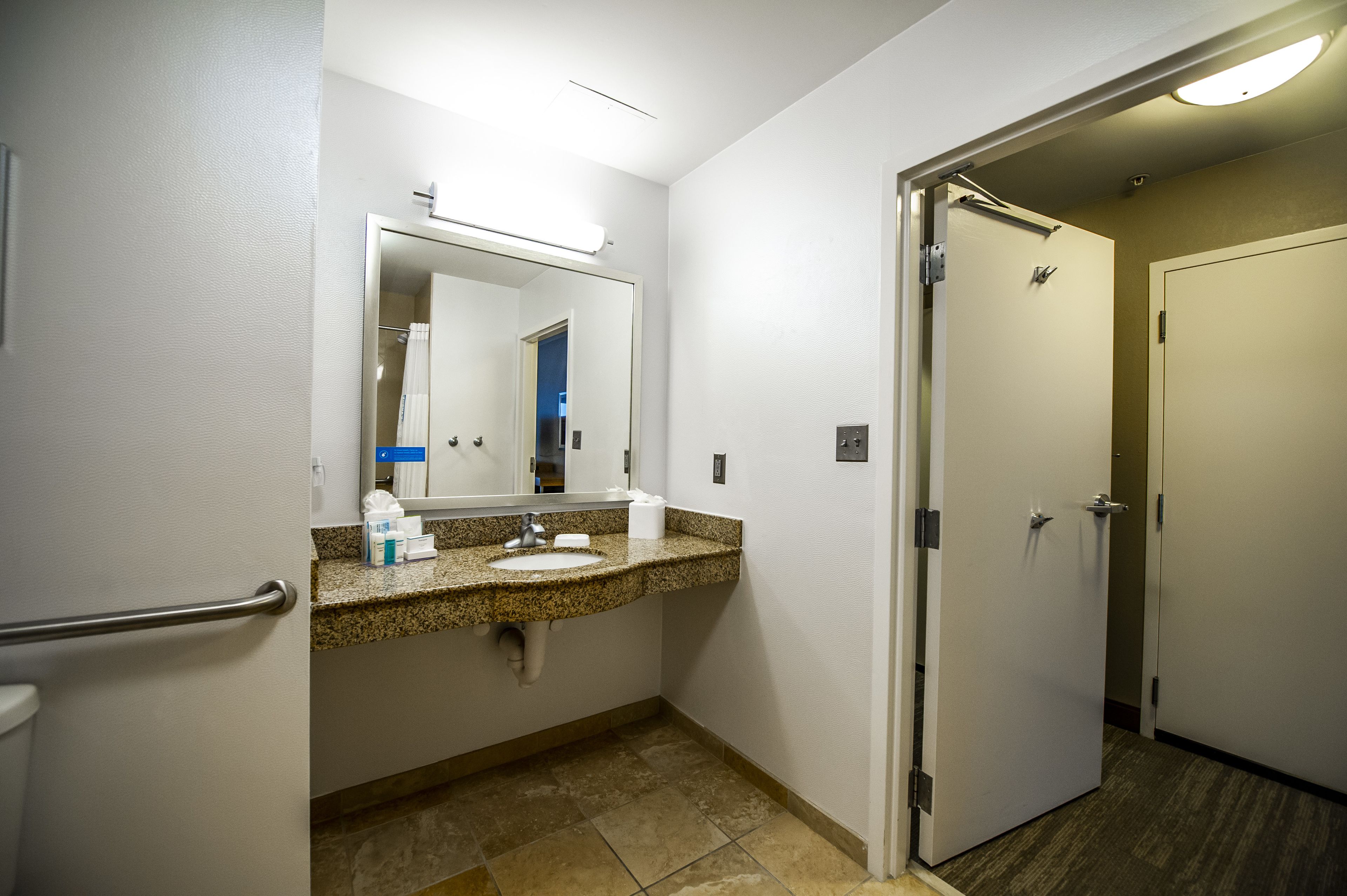 A hotel bathroom with a granite countertop sink, a mirror, and a toilet.