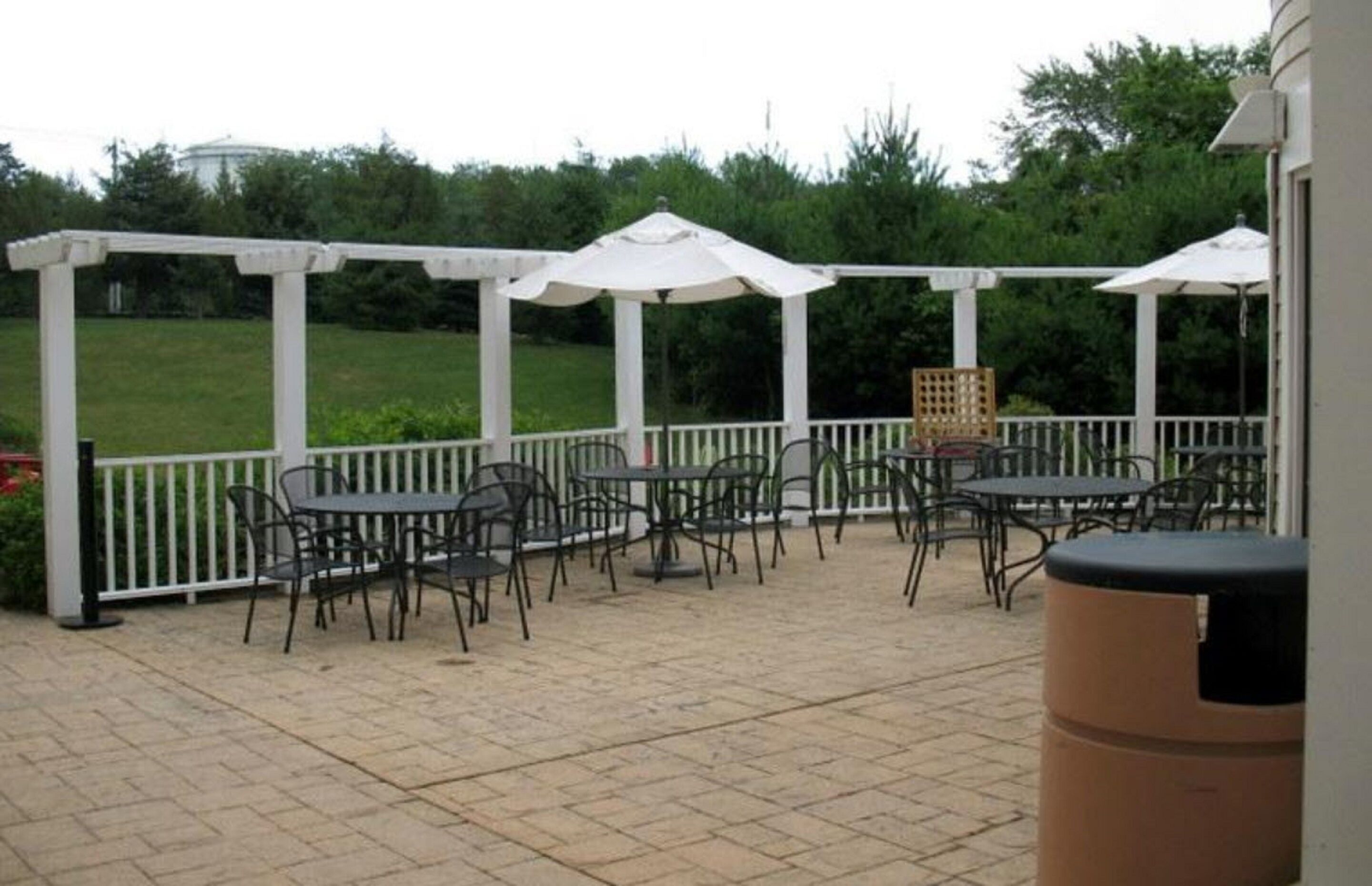 An outdoor patio with tables and chairs, white umbrellas, and a white fence.