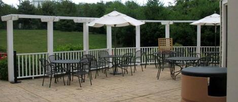 An outdoor patio with tables and chairs, white umbrellas, and a white fence.