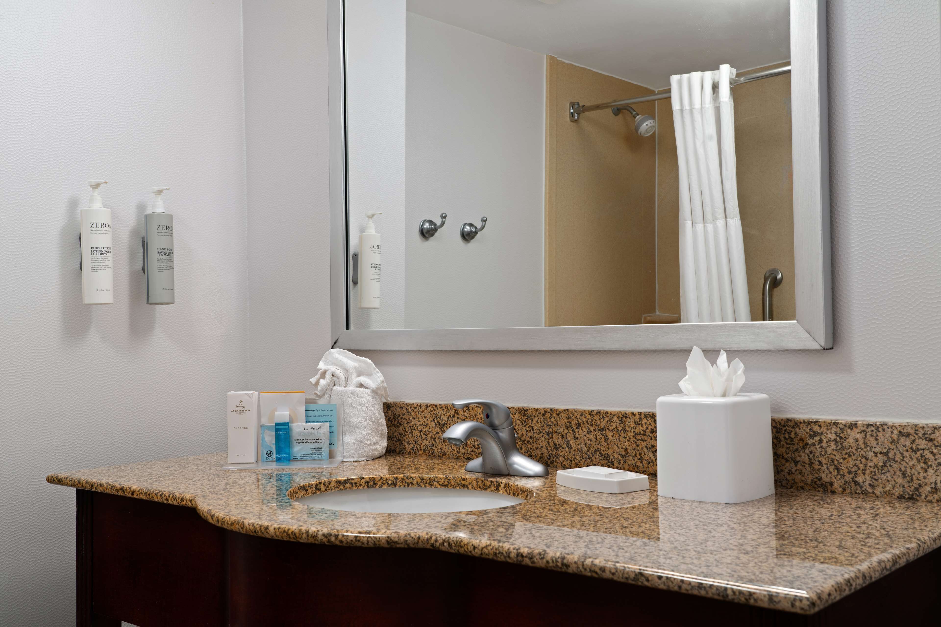 A bathroom with a granite countertop, a sink, a mirror, and toiletries.
