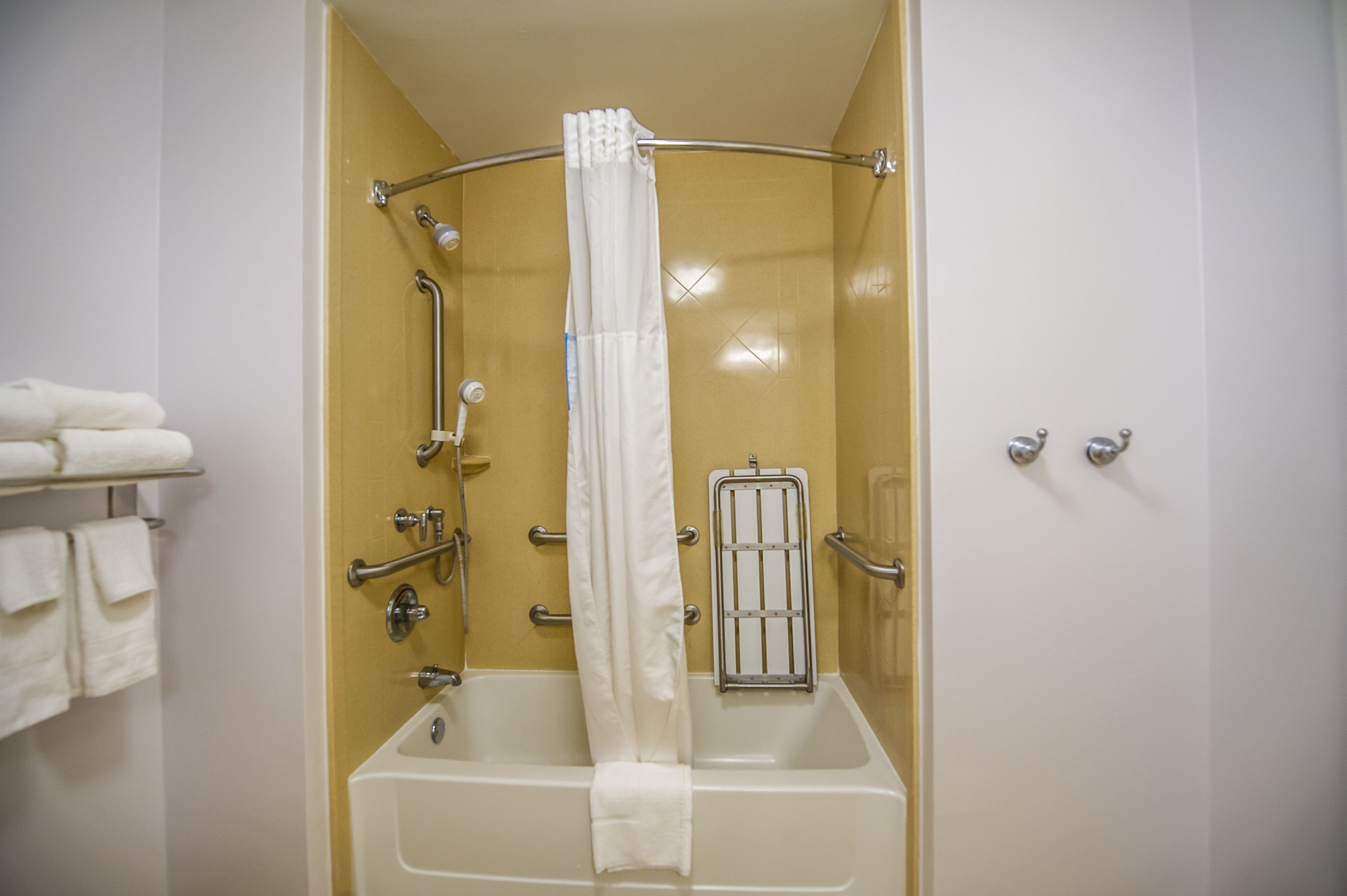 Une salle de bain avec une baignoire, une douche et des toilettes. Il y a des serviettes sur une étagère et un rideau est suspendu au-dessus de la baignoire.
